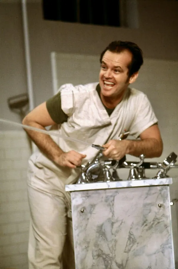 A man sprays water from a sink while smiling gleefully in One Flew Over The Cuckoo's Nest