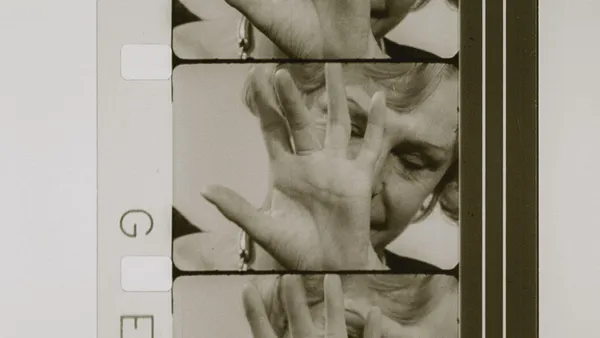 A vertical strip of black and white film showing an elderly white woman raising her hand, palm outwards, in front of her face.