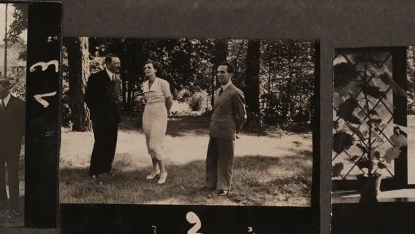 An old strip of black and white film depicting a white woman in a white dress standing in a garden between Adolf Hitler and another white man.