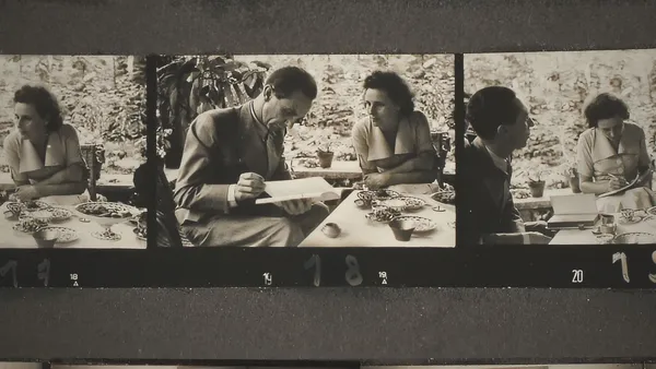 A strip of black and white film showing a white man and woman writing while taking tea on a veranda.