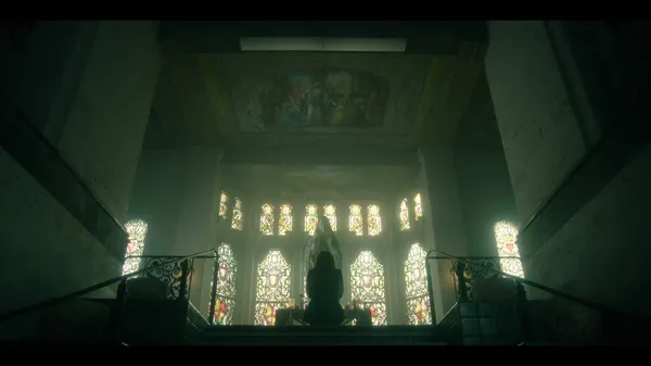 A still from the film Saint Clare. The silhouette of a woman can be seen praying beneath an enormous stained glass cathedral window.