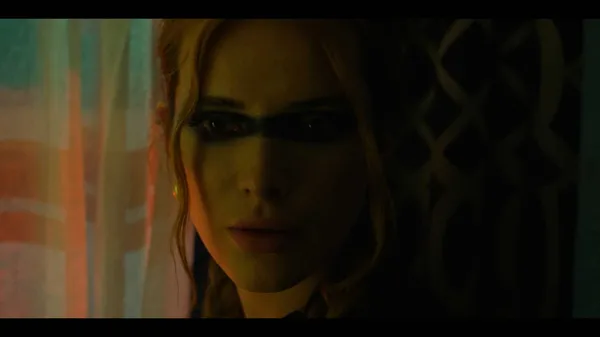 A still from the film Saint Clare. The face of a young red-haired white woman, half in shadow, with a black mask across her eyes.