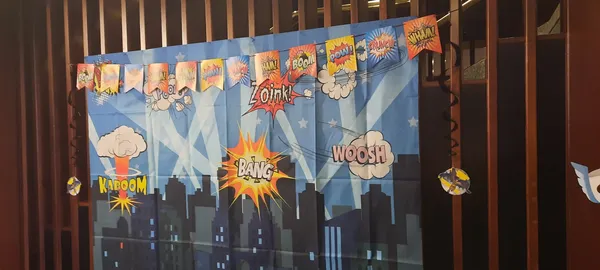 A photo backdrop hanging up on railings shows the Gotham City skyline along with the words bang, kaboom, zoink and whoosh.