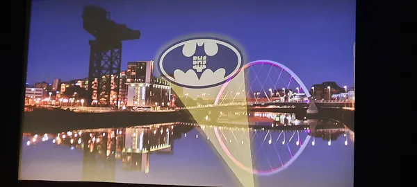 A cinema screen shows the River Clyde at night, with the bat signal projected over it.