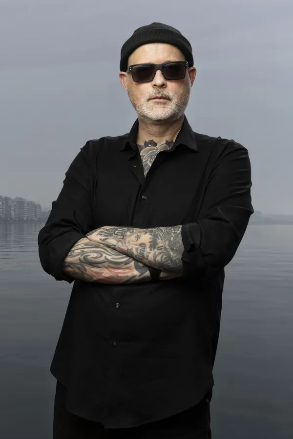 Director Denis Côté in Thessaloniki, all in black, he has glasses and a lot of tattoos. You can see the water behind him