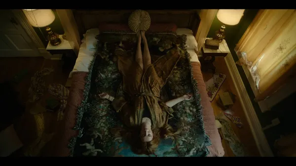 A still from the film Saint Clare. A young red-haired white woman lies on her back on a green embroidered rug.