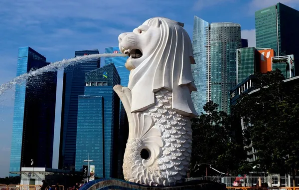 The famous merlion statue overlooking the main harbour in Singapore. A white statue of a creature with the head of a lion and the body of a fish, with water spouting out of its mouth.