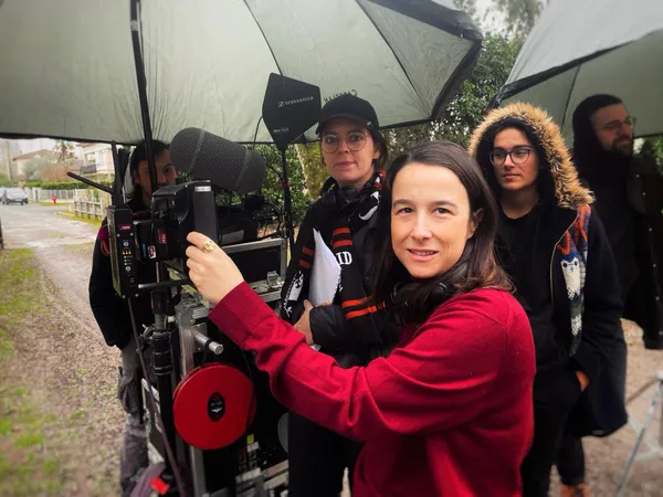 The film director Sarah Lasry, a brunette white woman in a red coat, working with her crew.
