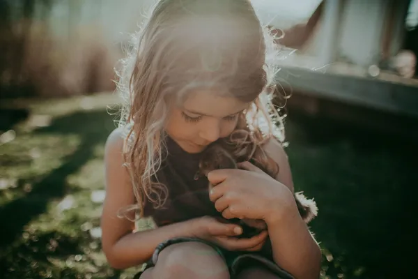 A still from the film A New Kind Of Wilderness. In a garden, a long-haired white child lovingly cradles a duckling.