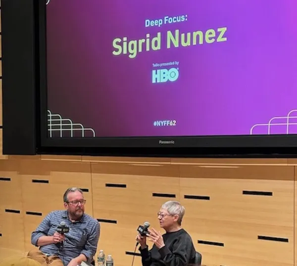 A white man and a white woman, holding microphones, site in front of a purple cinema screen which displays the name Sigrid Nunez.