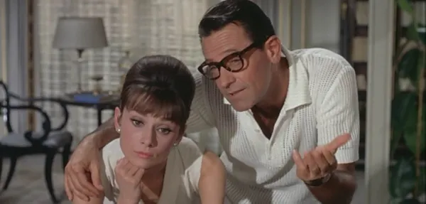 A still from the film Paris When It Sizzles. A dark-haired, bespectacled white man stands with his arm around a delicately built white woman with a neat beehive of brown hair.