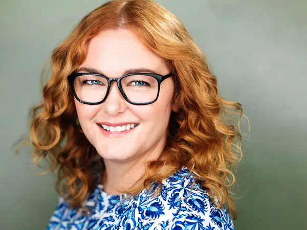 A bespectacled white woman with a bob of curly red hair and a wide smile.