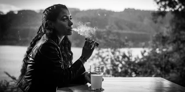 B&W shot of a woman sitting at a table smoking a cigarette