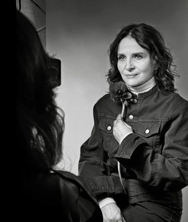 Juliette Binoche posing for a photo with a flower, she is wearing a dark jacket