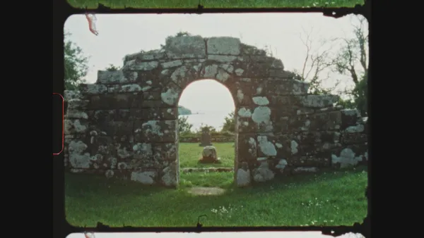 A still from the film Blue Road - The Edna O'Brien Story. A crumbling stone archway which looks as if it was once part of a building, in a grassy field.