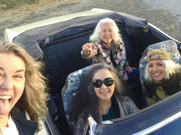 Bobbi Jo Hart, Jean Millington and June Millington with Brie Howard Darling driving a convertible