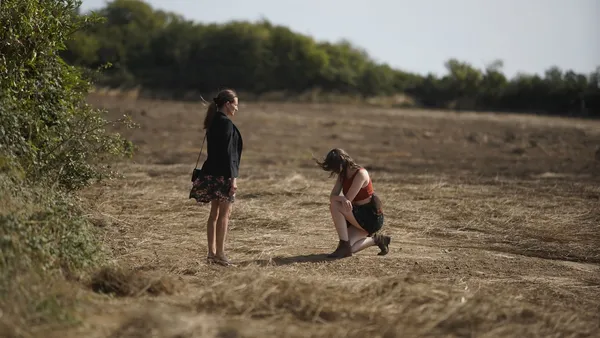 Camille Cottin and Anamaria Vartolomei. Two white women on a patch of sandy ground, hemmed in by trees.
