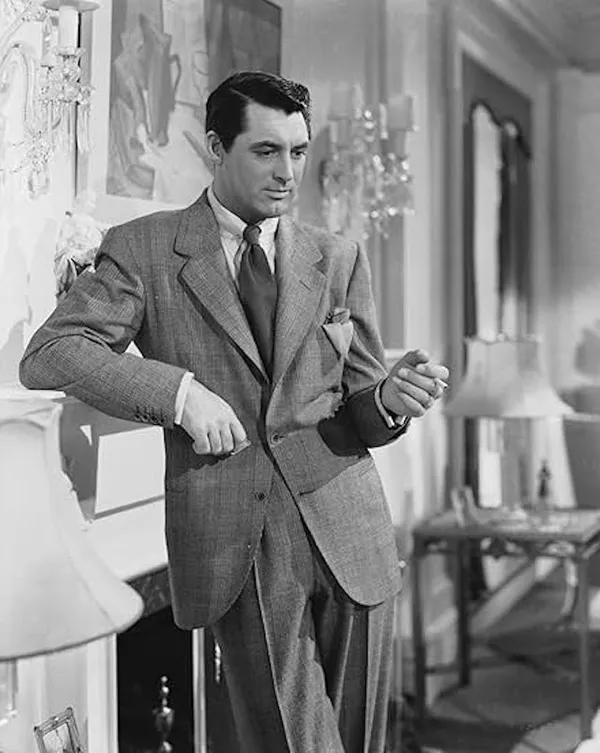 A still from the film Suspicion. A white man in stylish 1940s clothing leans against a fireplace. The positioning of a painting behind him makes it look as if he is being stabbed in the back of the neck by a knife.
