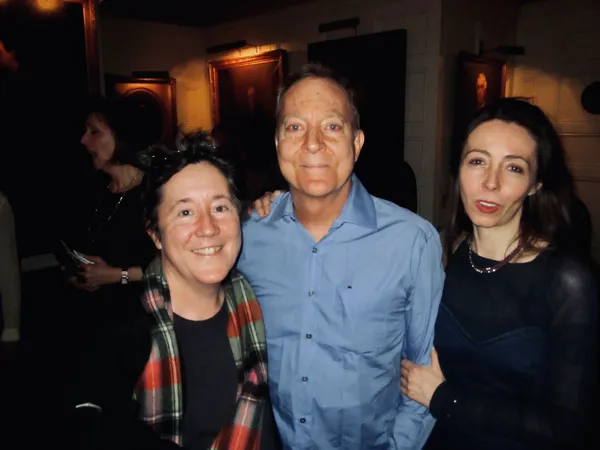 A white man and two white women stand together, smiling, in a bar.