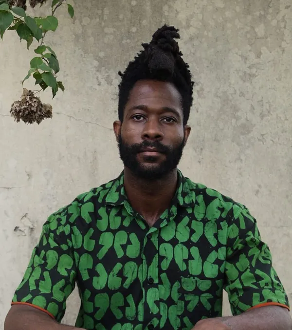 The filmmaker Chuko Esiri. A bearded Black man with hair piled in a high cone atop his head, wearing a black shirt with a green pattern.