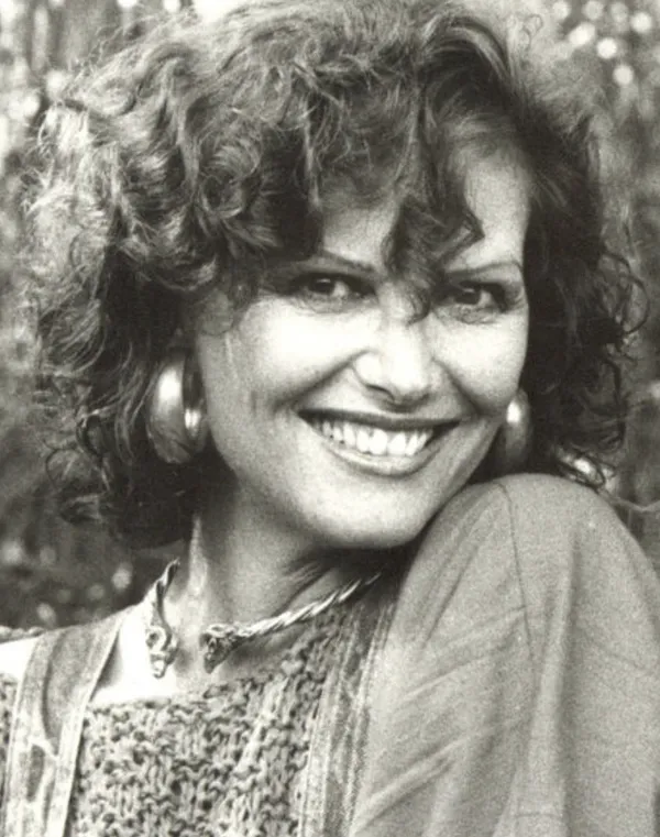 A black and white picture of the actor Claudia Cardinale. A middle aged woman with curly hair, thick hoop earrings and a mischievous grin.