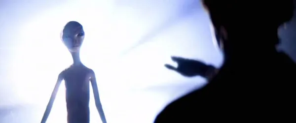 A still from the film Close Encounters Of The Third Kind. A slender alien figure with large, dark eyes emerges from a bright white light.