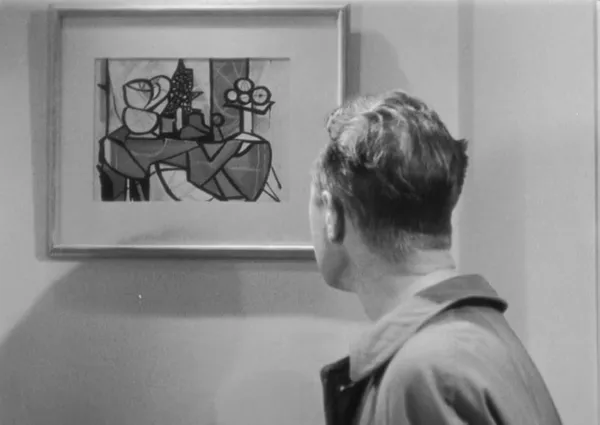 A black and white still from the film Suspicion. A white man, seen from behind, regards a modernist still life painting.