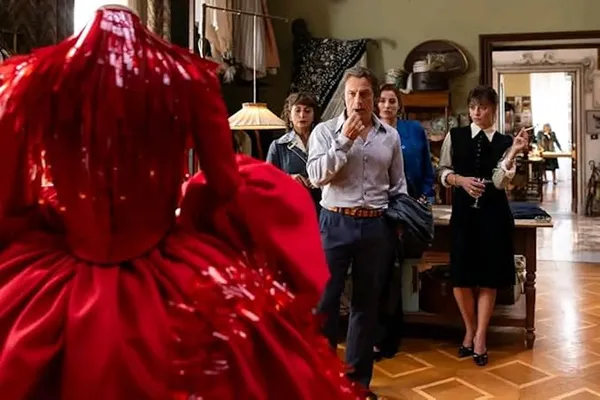 A still from the film Diamonds. In a dressmaking studio, a white man and three white woman critically observe a voluminous red dress. One of the women is holding a cigarette.