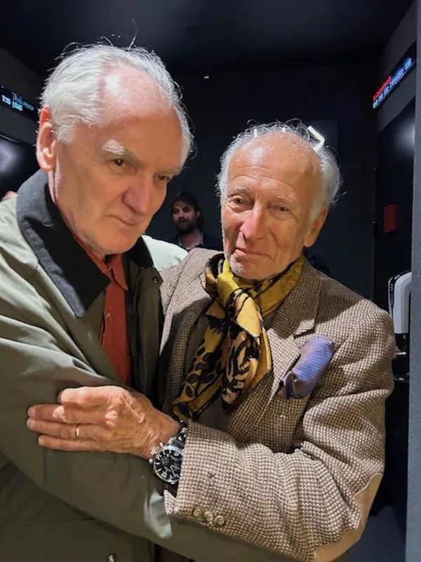 Two older white men hug in a corridor.