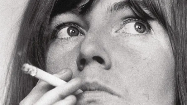 Edna O'Brien, in black and white. A close-up of the face of a white woman whose dark eyes look searching and slightly paranoid as she smokes a cigarette.