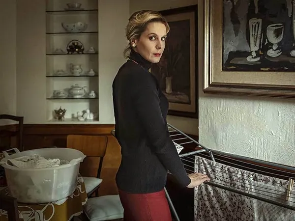 A still from the film The Great Ambition. An elegant middle-aged white woman hangs laundry on a frame.