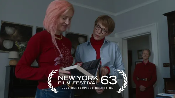 A still from the film Father Mother Sister Brother. Two white women look at a book together while an older white woman watches from the door of the room.