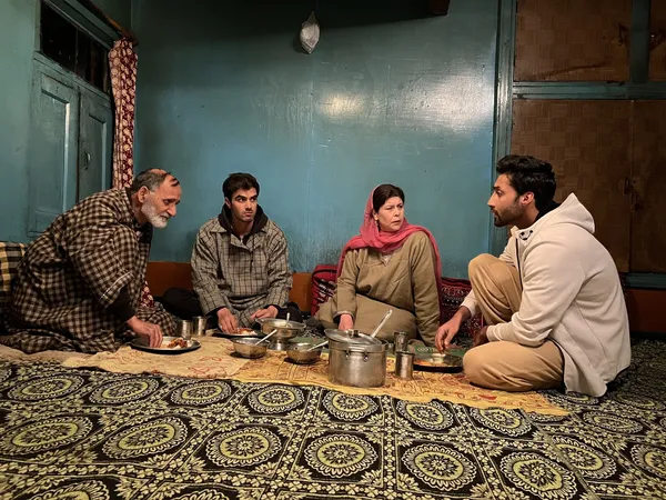 A still from the film We Are Faheem & Karun. A Kashmiri family - an older man and woman and their two twenty something sons - sit on the floor of their blue-walled home to eat dinner.