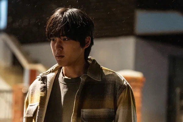 A still from the film Fragment. A young Korean man stands in the street on a snowy night, looking depressed.