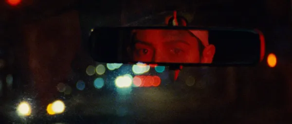 A still from the film Gazer. A young woman's eyes are reflected in her mirror as she drives through traffic at night.