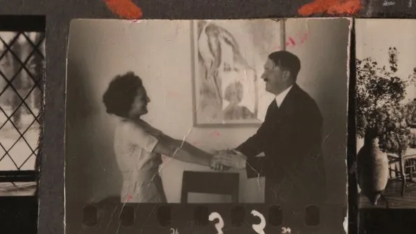 An old black and white photograph showing a white woman extending her arms towards Adolf Hitler in a warm gesture of welcome, in a domestic room.