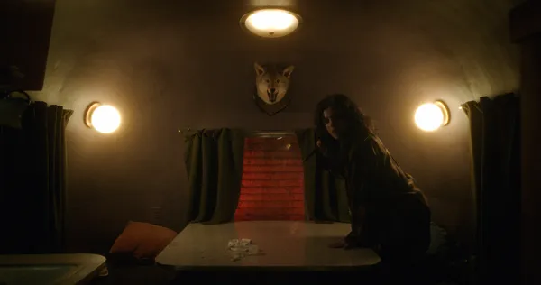 A still from the film Hellcat. A young white woman stands in an RV, resting her hands on a central table overlooked by a mounted wolf's head.