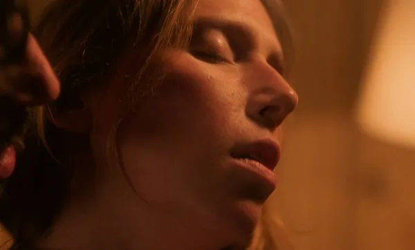 A still from the film Hotel Acropole. A man with light brown skin whispers into the ear of a white woman as she tilts her head and closes her eyes.
