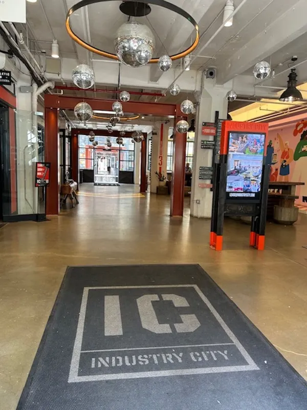 A succession of wide corridors with smooth stone floors, with glitterballs hanging overhead. A large welcome mat bears the words 'IC Industry City'.