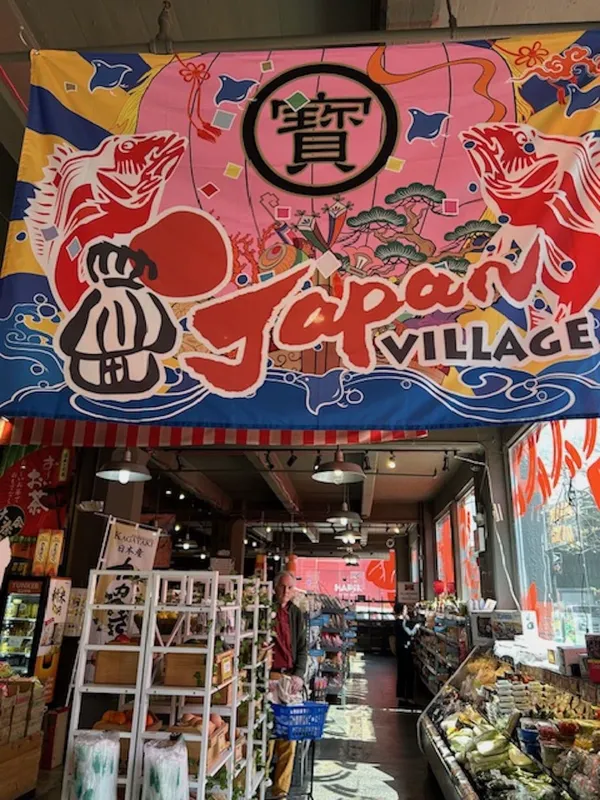 An older white man shops in a crowded marketplace with banner up above it emblazoned 'Japan Village'.