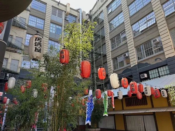 Red and white lanterns are strung across a courtyard between tall modern buildings, alongside painted fish.