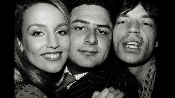 A black and white close-up of the faces of Johnny Pigozzi, Jerry Hall and Mick Jagger, close together.