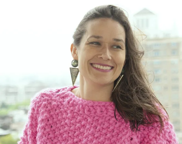 A smiling white woman with long brown hair, wearing a pink jumper.