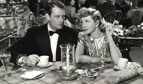 A still from the film The Palm Beach Story. A woman white woman cosies up to a politely resentful-looking white man as they sit at a restaurant table.