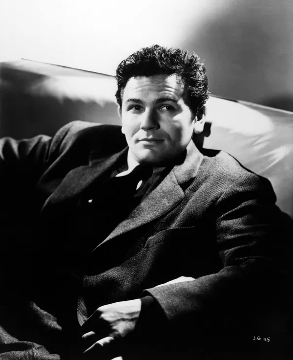 A dark-haired white man, wearing a dark suit, lounges in a booth.