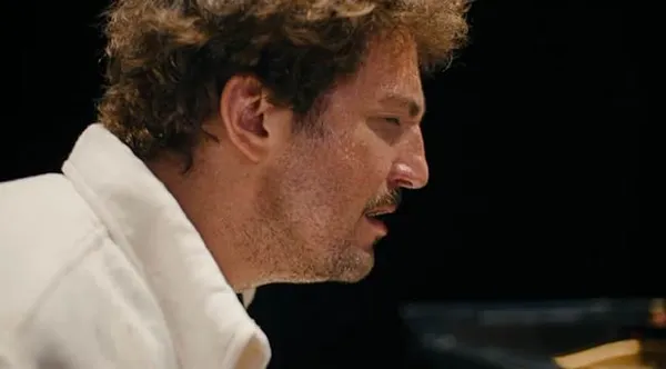 The face of a curly-haired white man with protruding stubble, seen from the side.