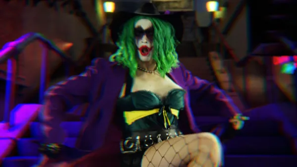 A still from the film The People's Joker. A mid-shot of a green-haired white woman in clown make-up, a corset, a purple coat and fishnets dancing on an outdoor flight of stairs.