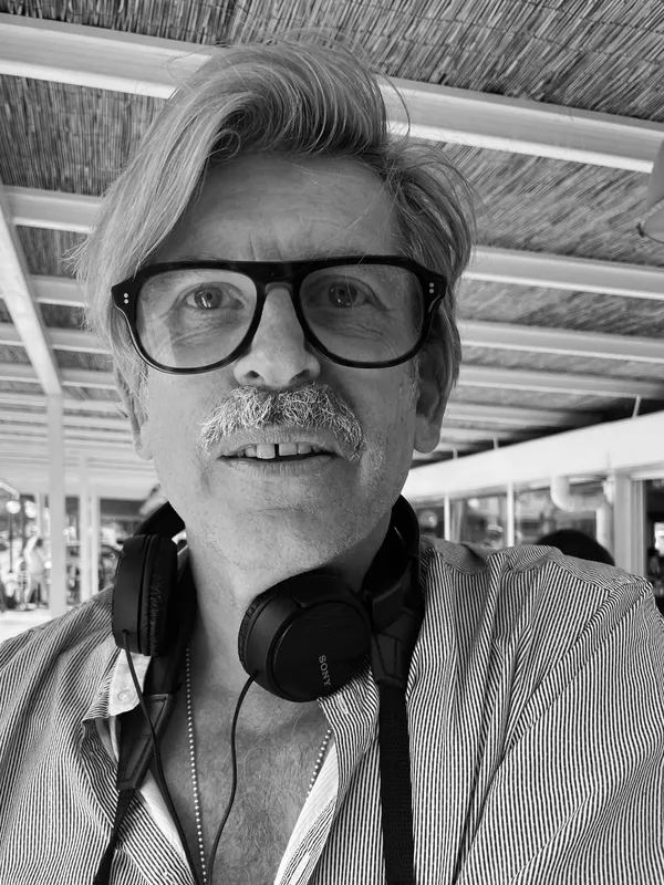 Justin Anderson. A black and white photograph of a fair-haired, bespectacled white man wearing headphones around his neck.