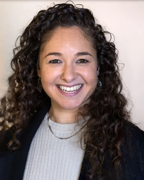 A middle aged woman with light brown skin and long dark curly hair.