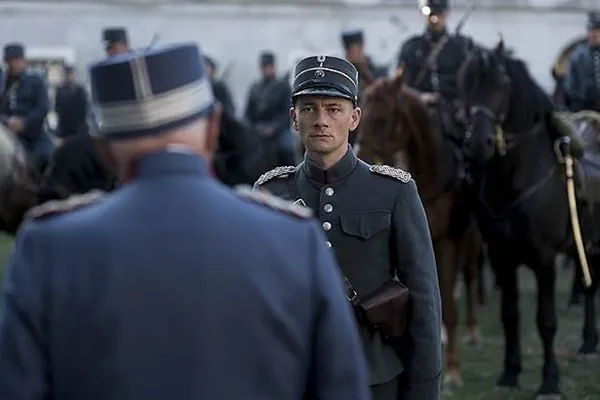 A still from the film The Kiss. Two middle aged white military men face one another. One has three rows of uniformed horsemen behind him.